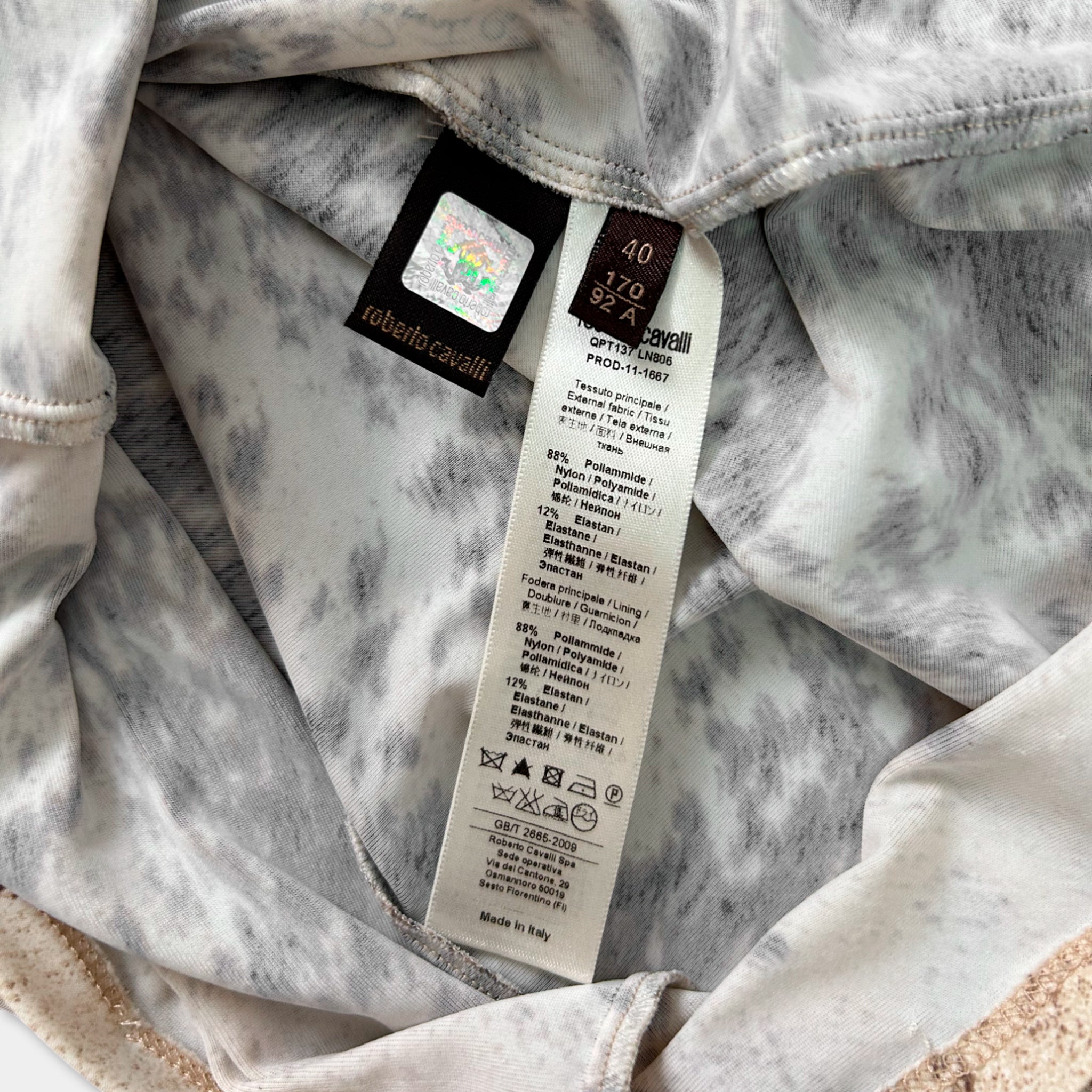 a close-up view of a fabric with a label attached to it, which contains text and symbols related to the product's care instructions and origin.