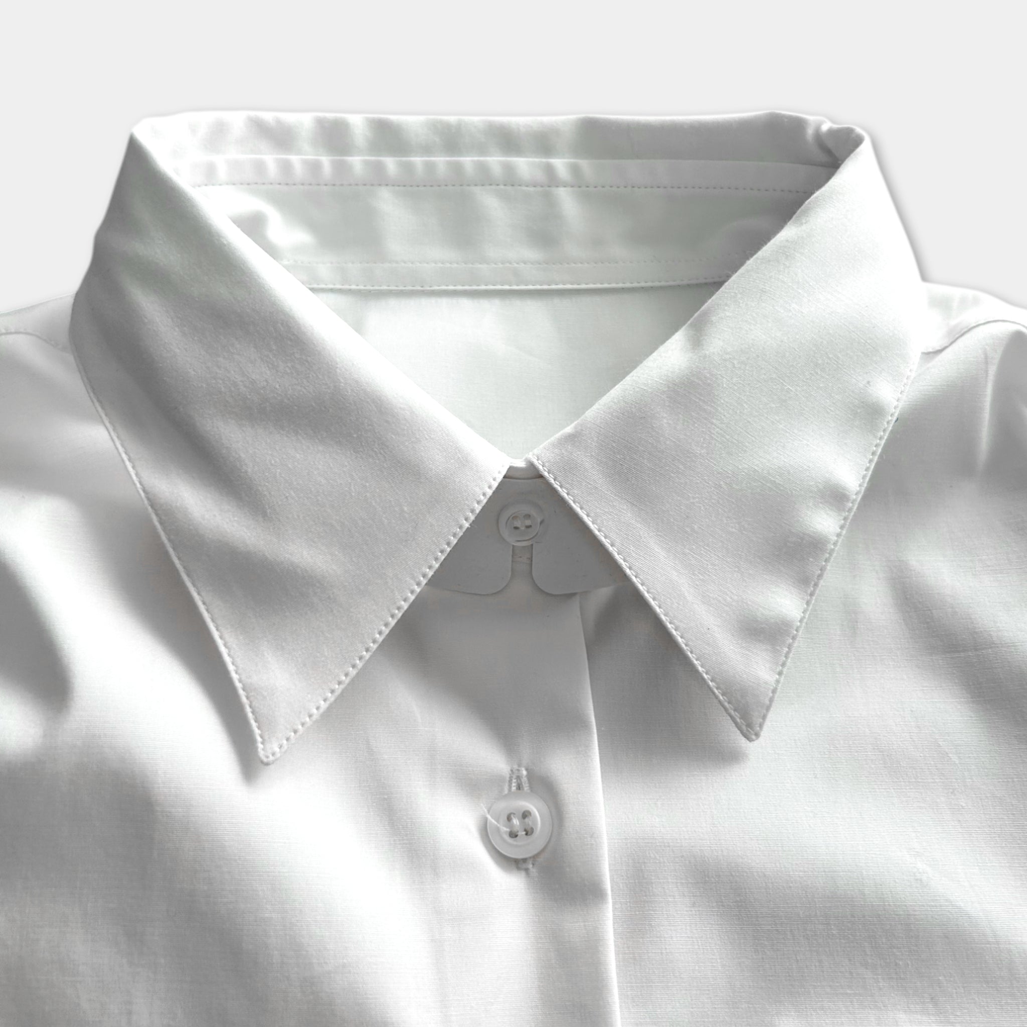 A close-up view of a white collared shirt, focusing on the collar and buttons.