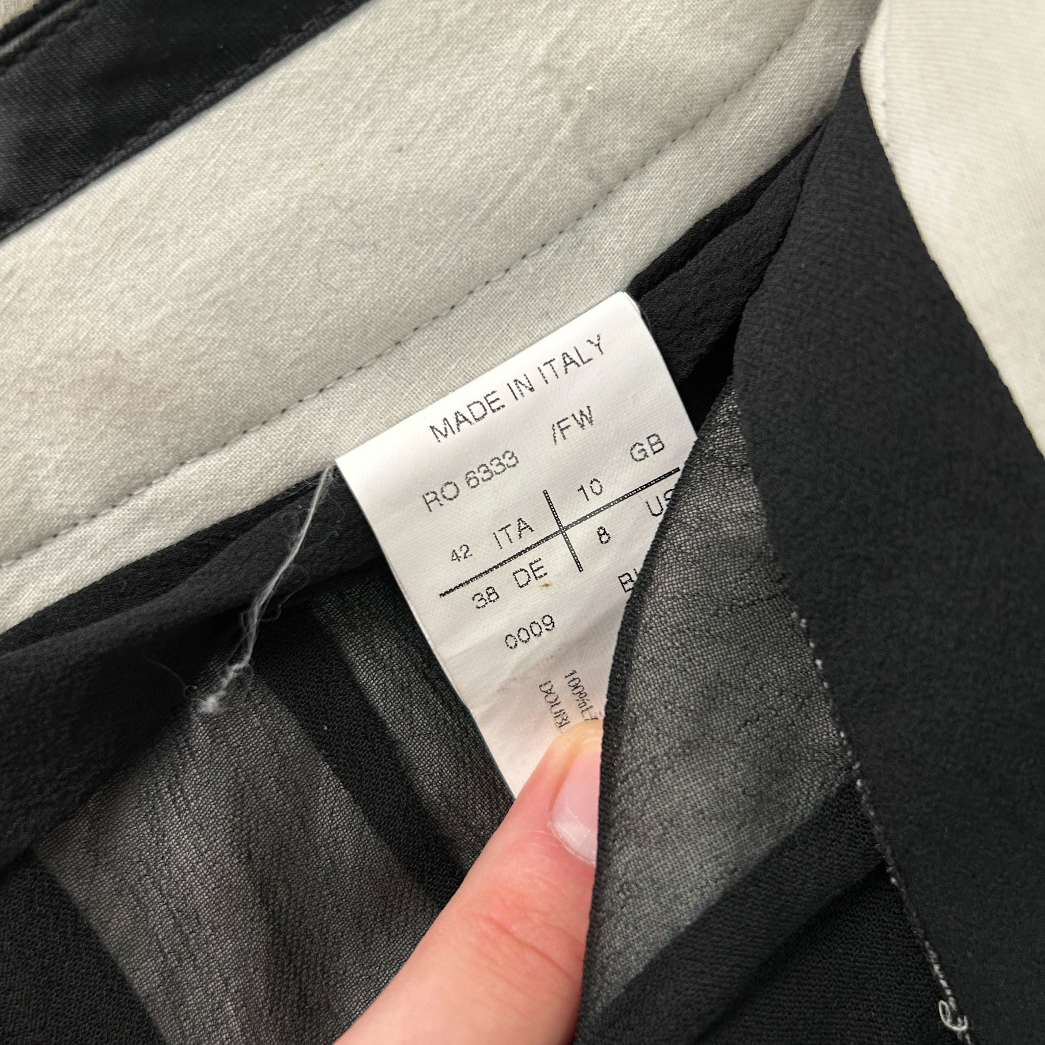 a close-up view of a label on a piece of clothing, with a person's hand holding it.