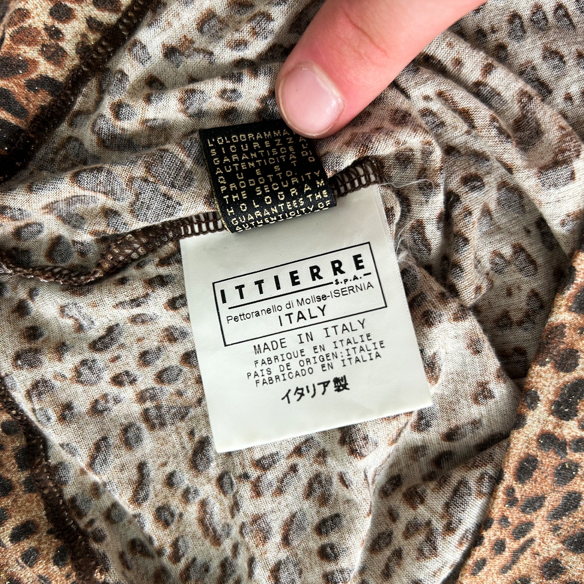 A close-up view of a hand holding a label with text on it, placed on a leopard print fabric.