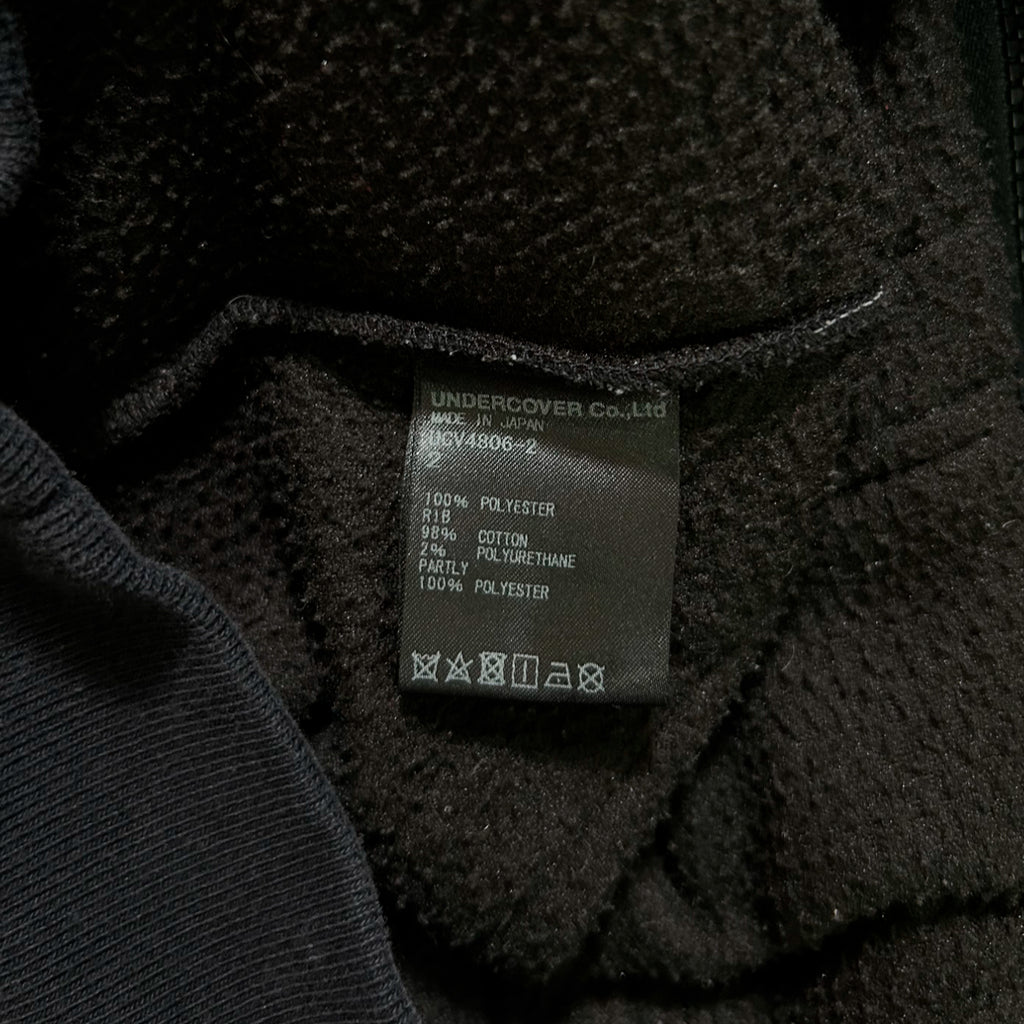 a close-up view of a black fabric, possibly a sweater or a jacket, with a label or tag attached to it. The label appears to contain information about the fabric, such as the material and care instructions.
