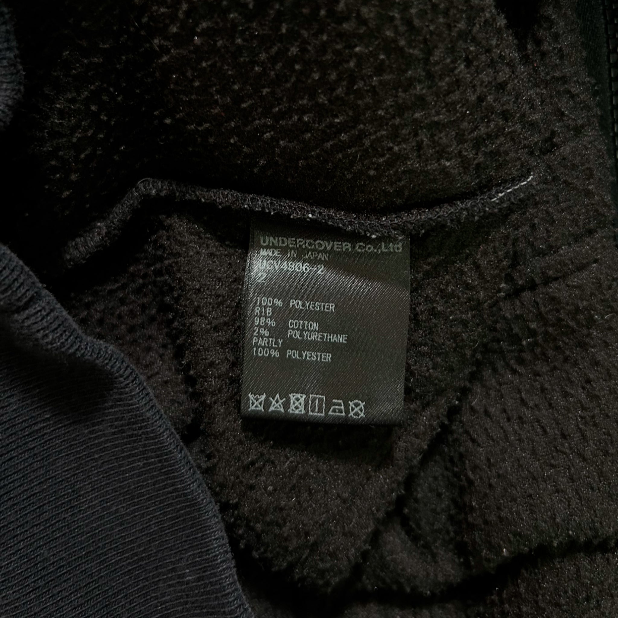 a close-up view of a black fabric, possibly a sweater or a jacket, with a label or tag attached to it. The label appears to contain information about the fabric, such as the material and care instructions.
