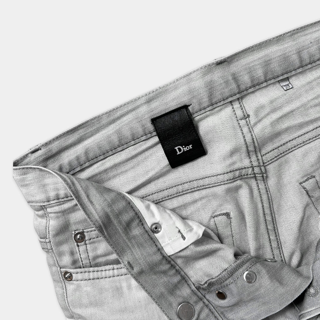 A pair of gray jeans with a Dior brand tag attached to the waistband.