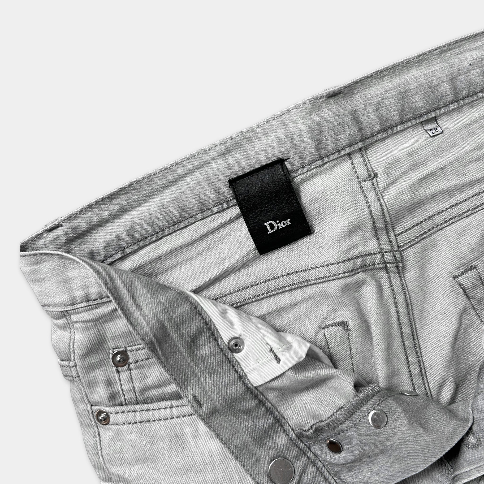A pair of gray jeans with a Dior brand tag attached to the waistband.