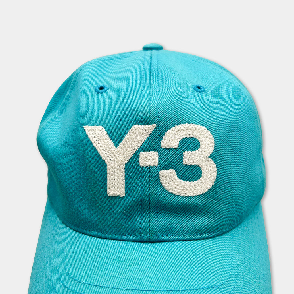 A turquoise baseball cap with the text "Y-3" embroidered on it.