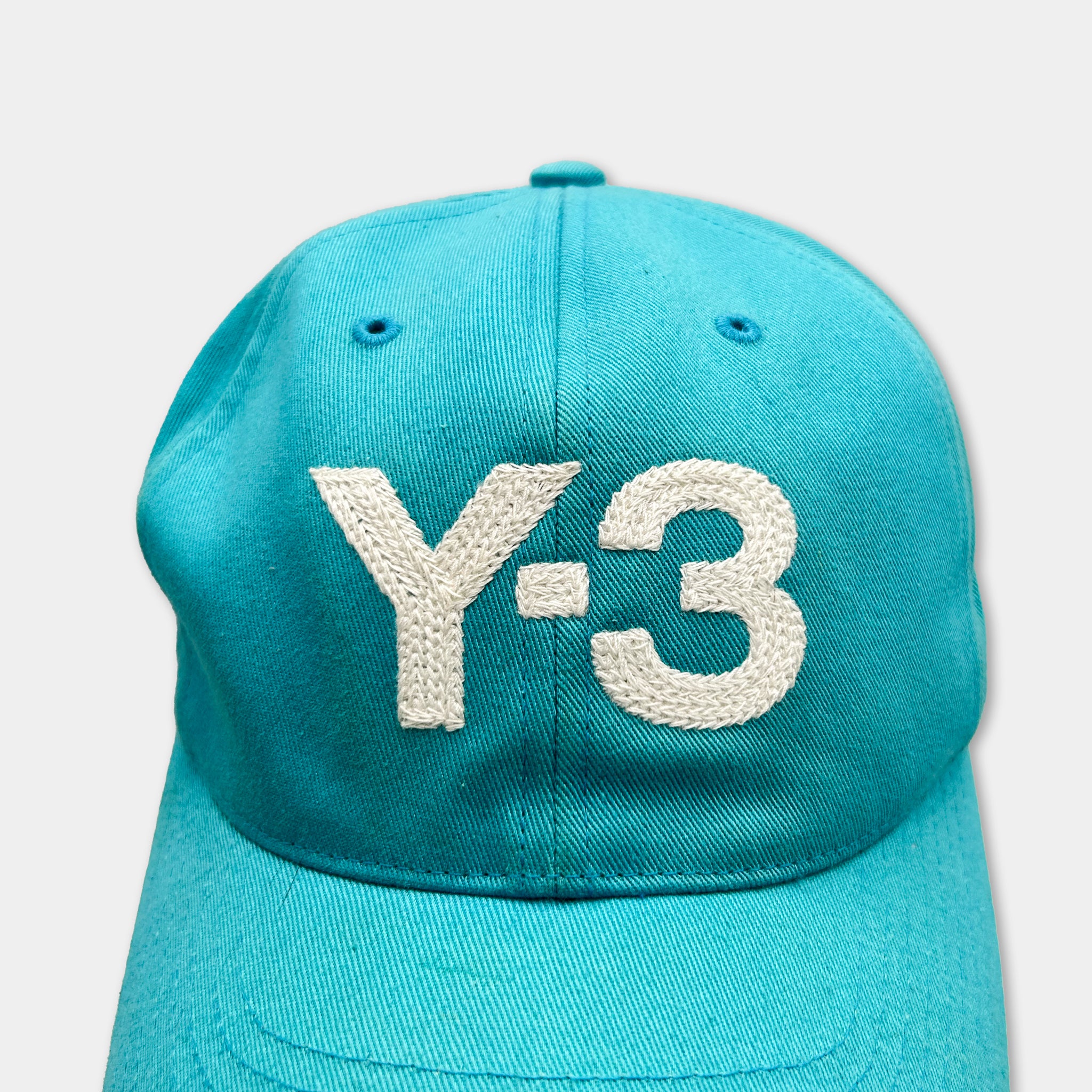A turquoise baseball cap with the text "Y-3" embroidered on it.