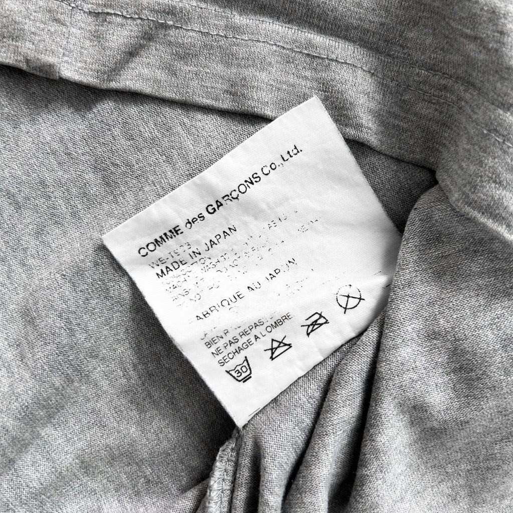 a close-up view of a grey fabric, possibly a garment or textile, with a label attached to it. The label appears to contain text and symbols related to the garment's care instructions or origin.