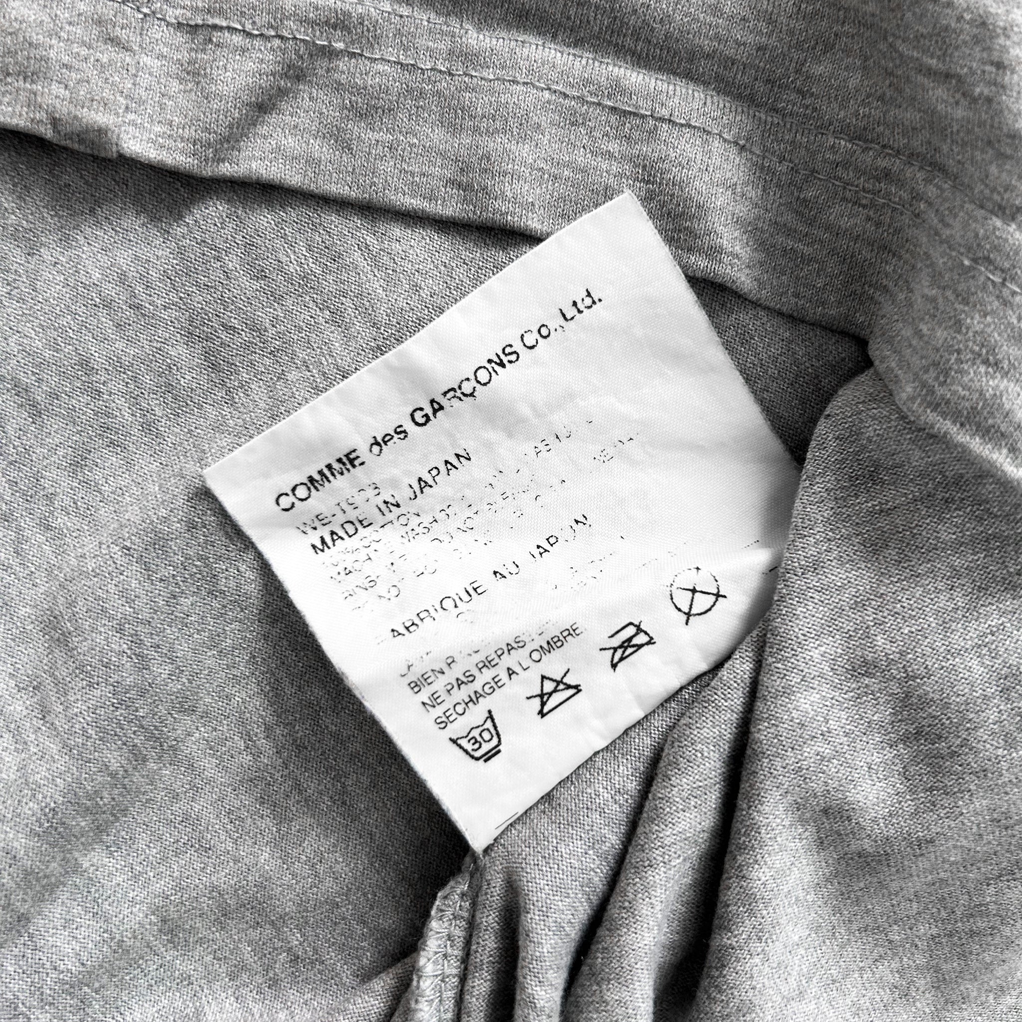 a close-up view of a grey fabric, possibly a garment or textile, with a label attached to it. The label appears to contain text and symbols related to the garment's care instructions or origin.