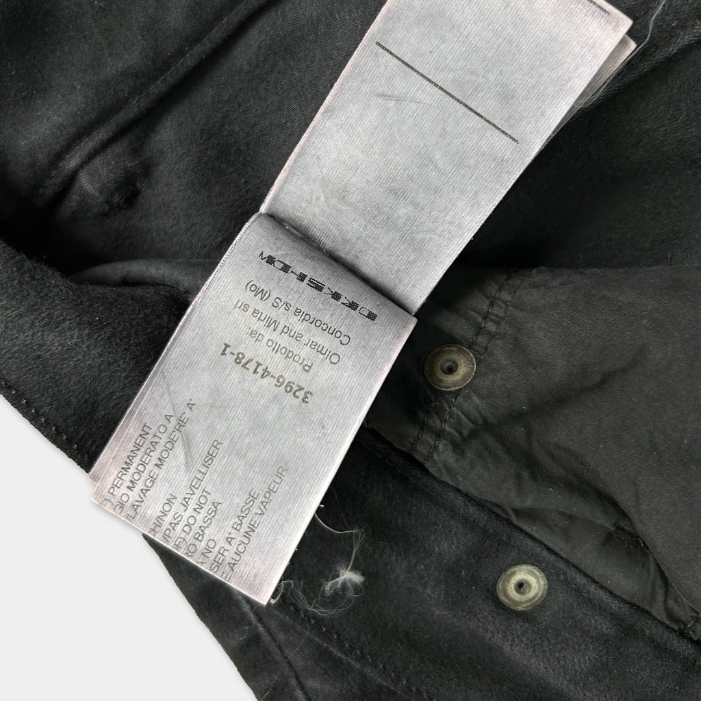 a close-up view of a black fabric, possibly a piece of clothing, with a label attached to it. The label appears to contain text and instructions related to the garment, but the exact wording is not clearly visible due to the angle and focus of the photograph.