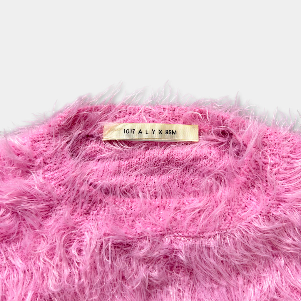 A close-up image of a pink fuzzy sweater with a label on the back.