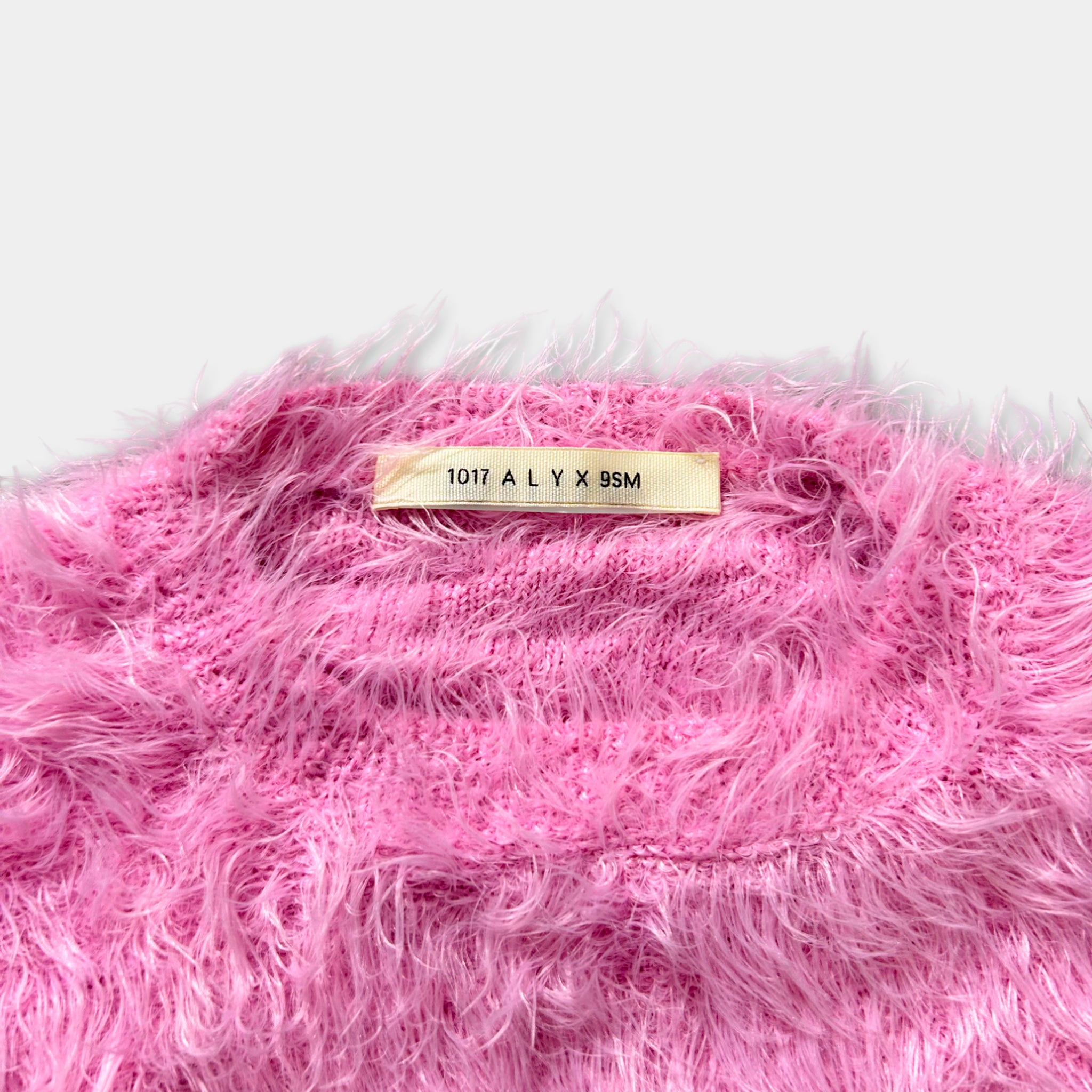 A close-up image of a pink fuzzy sweater with a label on the back.
