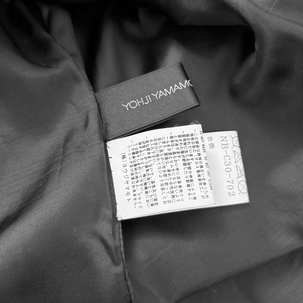 A close-up black and white image of a fabric label with text in Japanese, attached to a fabric.