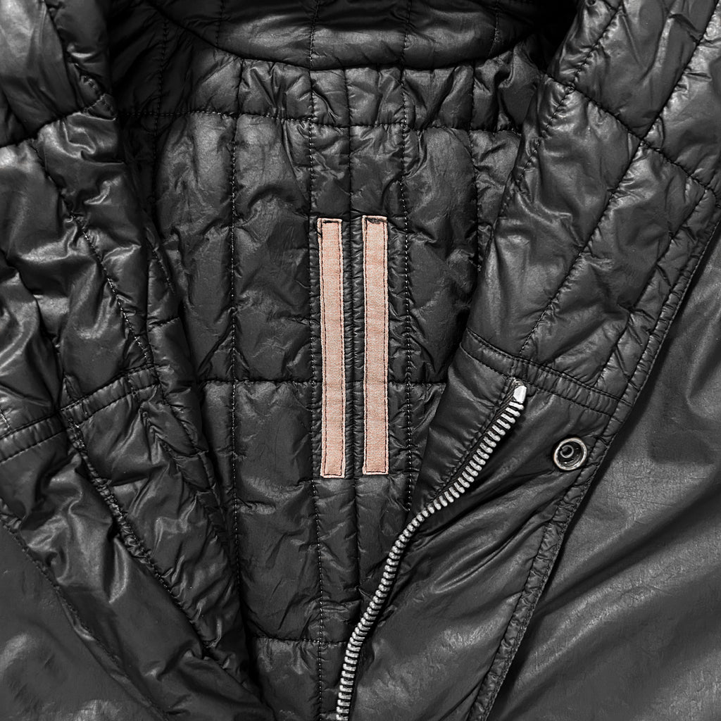 A close-up view of a black, padded jacket with a zipper and a small pink patch on the left side.