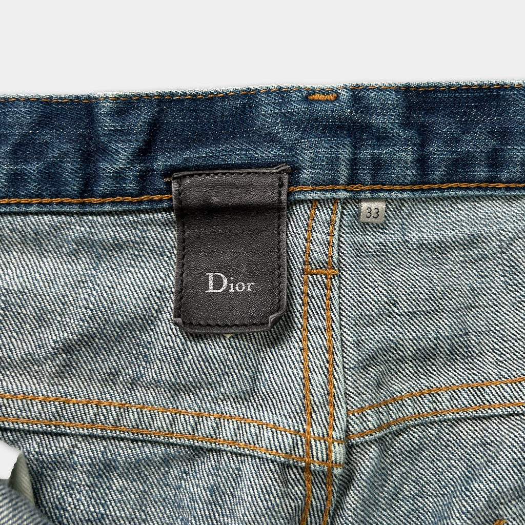 a close-up view of a denim pocket on a pair of jeans, with a Dior brand label attached to the pocket.