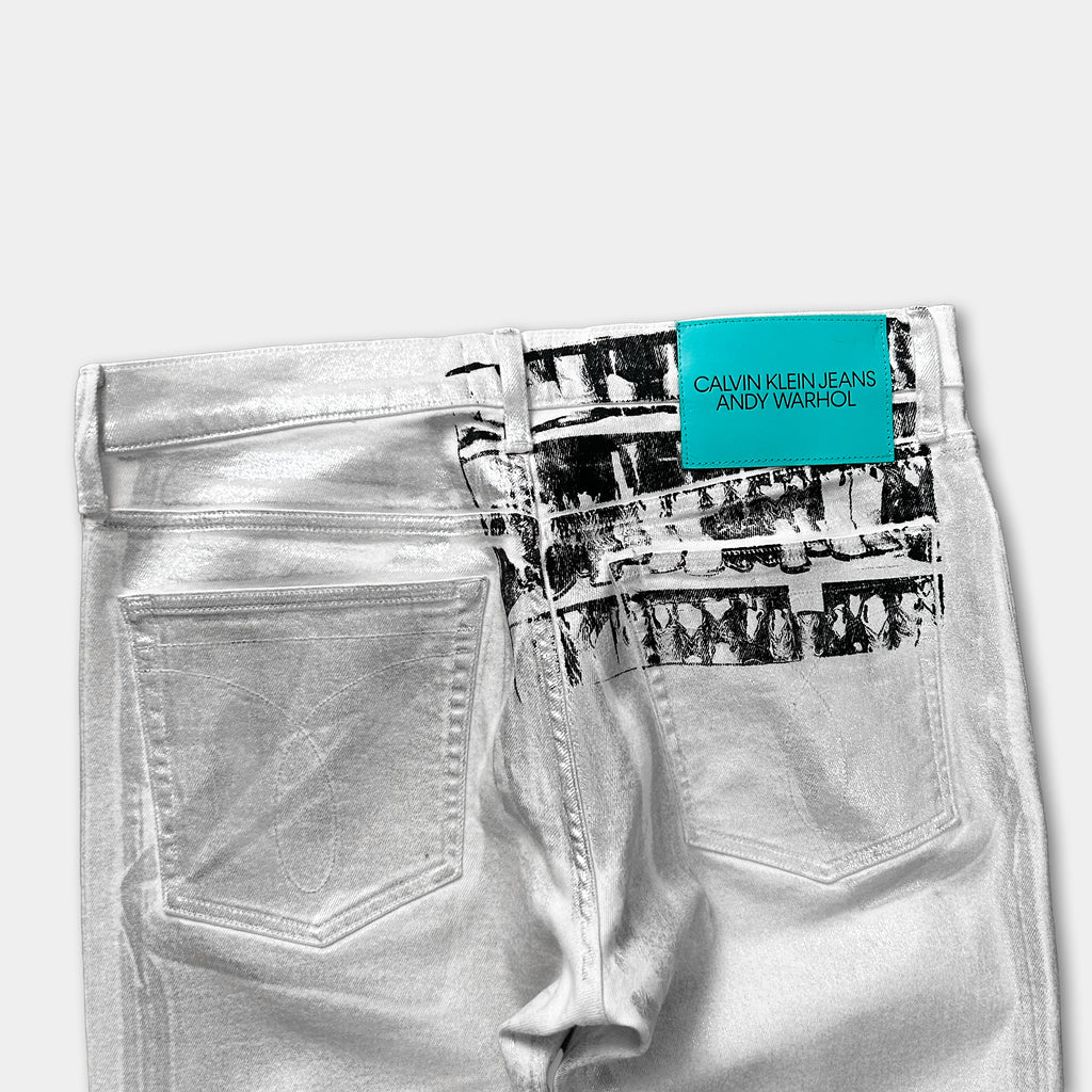 A pair of white Calvin Klein Jeans with a label that reads "Calvin Klein Jeans Andy Warhol" printed on the back pocket area.