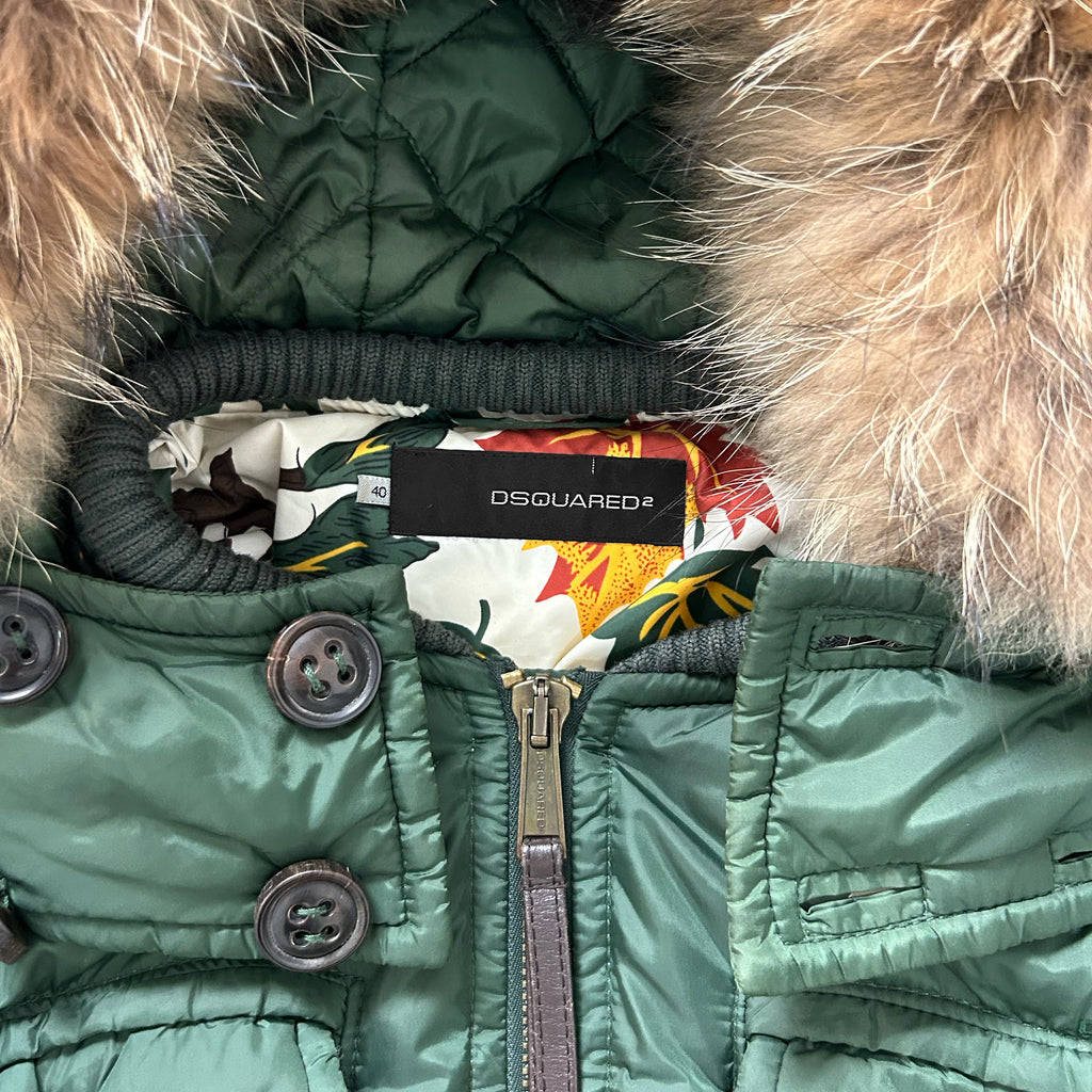 A close-up view of a green jacket with a fur-lined hood and a label on the collar.