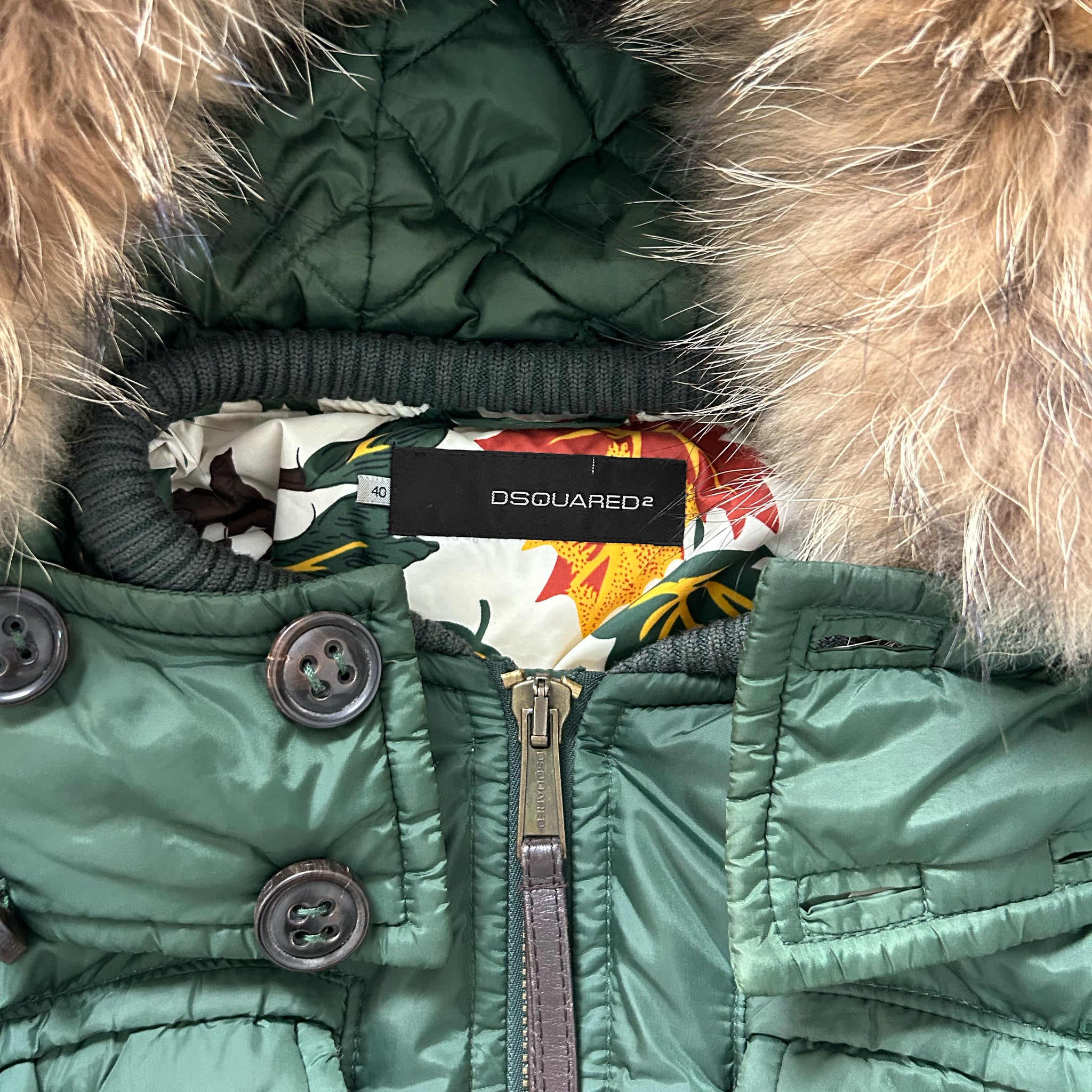 A close-up view of a green jacket with a fur-lined hood and a label on the collar.