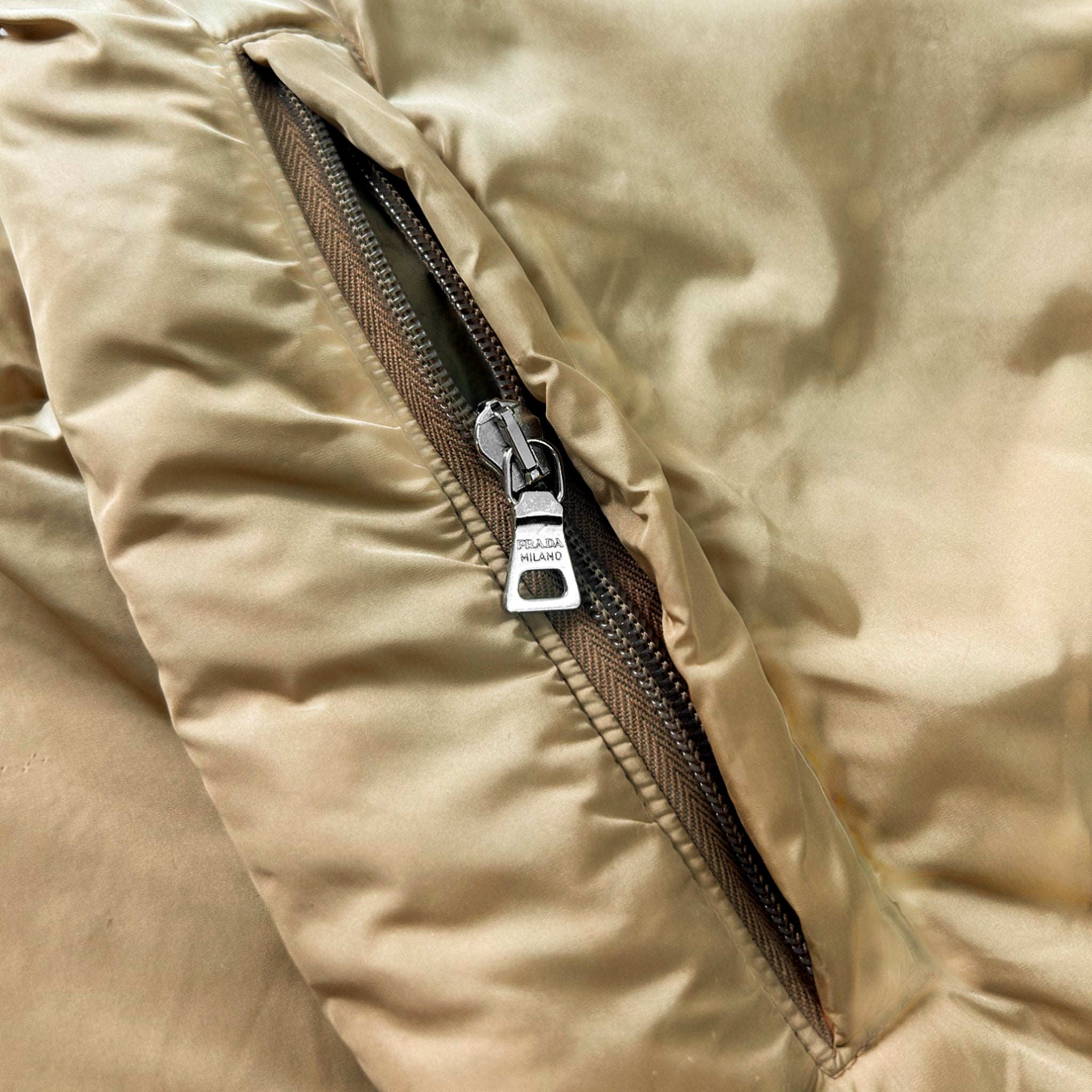 A close-up view of a zipper on a beige fabric, with a metallic zipper pull visible.
