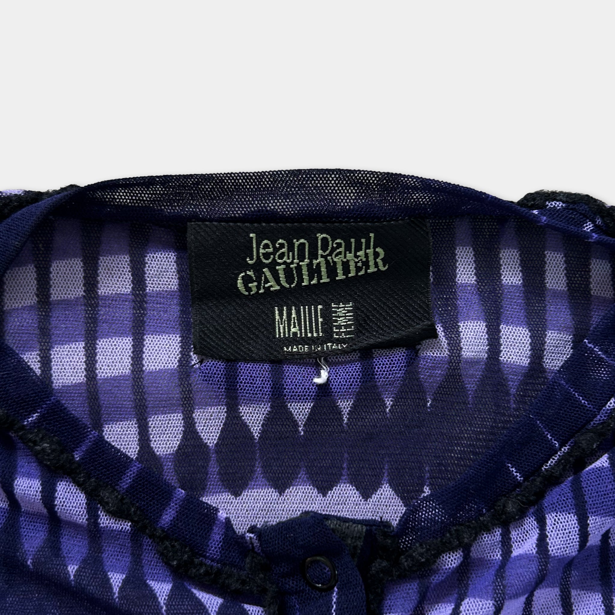 a close-up view of a purple and black patterned fabric, with a label attached to it that reads "Jean Paul Gaultier MAILIE FRANCE".