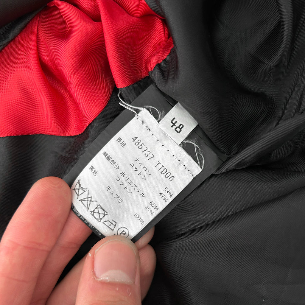 A close-up view of a black and red fabric, with a label attached to it. The label appears to contain text and symbols, possibly related to the fabric's care instructions or identification number.