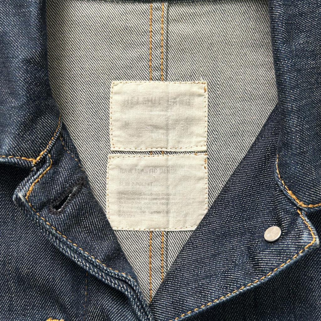 a close-up view of a denim jacket, focusing on the collar and the label attached to it.