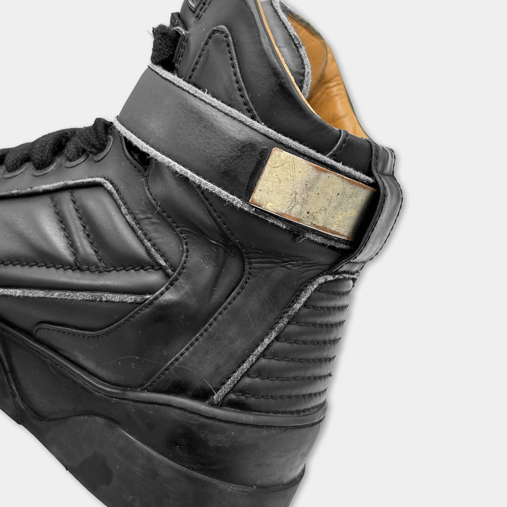 A close-up view of a black leather sneaker with a distinctive design and a label on the side.