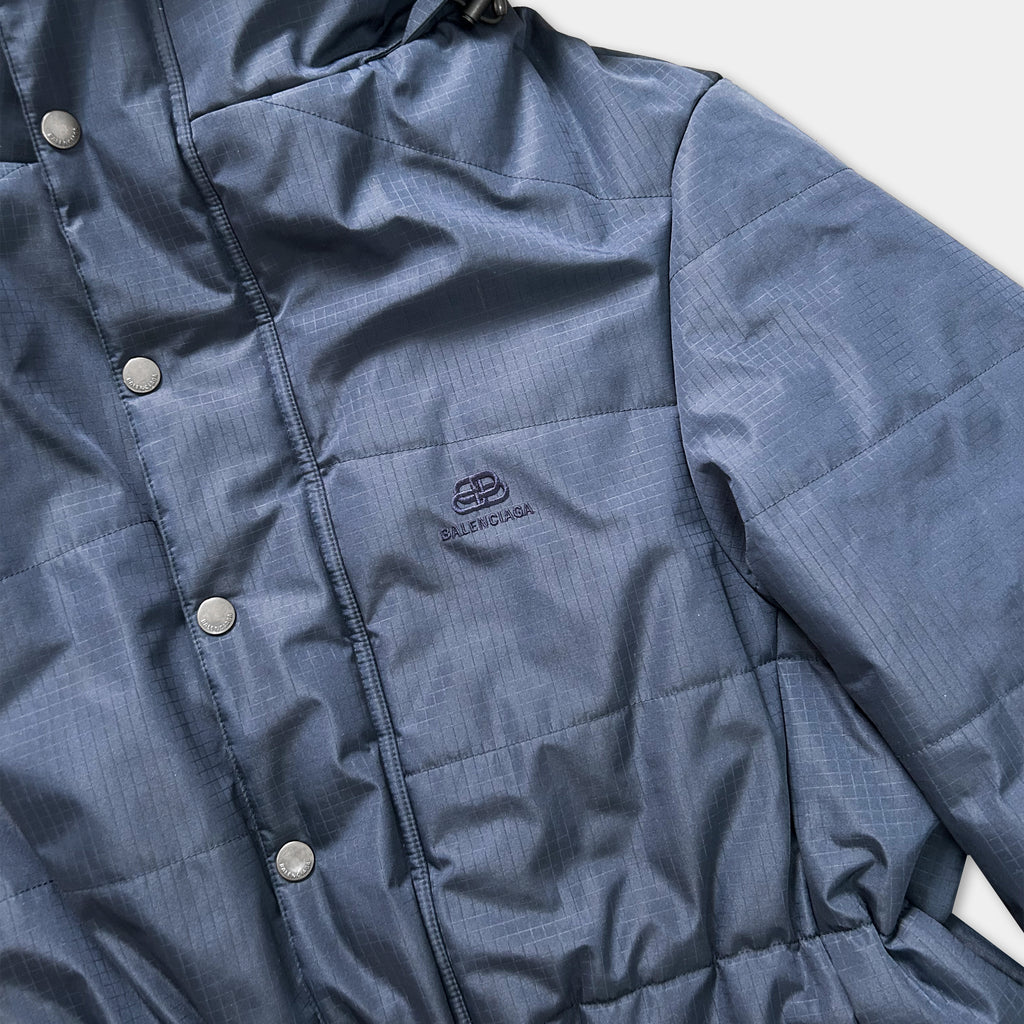 A close-up view of a blue puffy jacket with buttons, showing the brand logo and design details.
