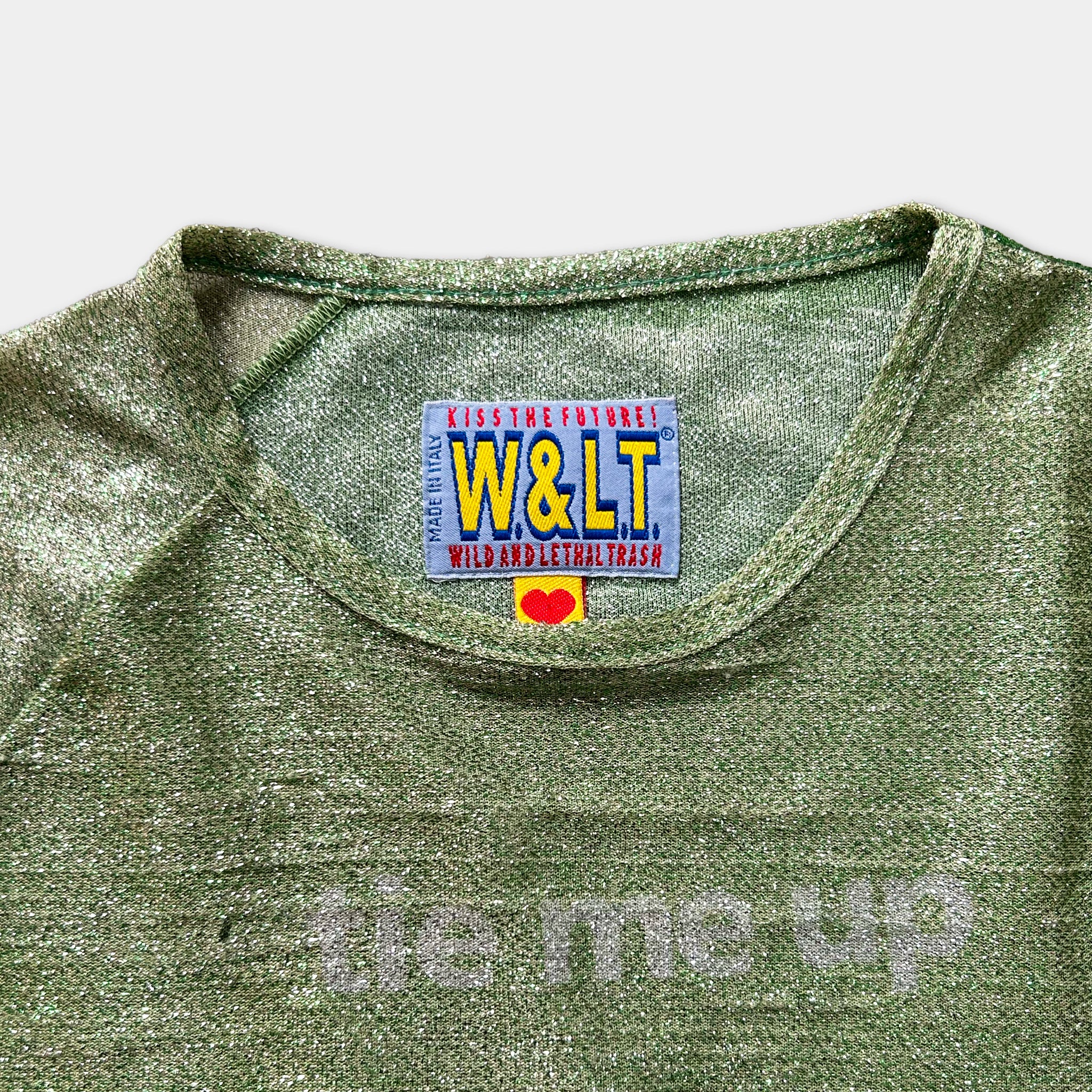 A green t-shirt with a label on the collar that says "KISS THE FUTURE W&LT WILD AND LETTER TRASH".