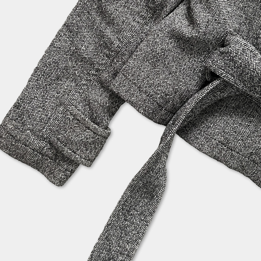 A close-up view of a grey tweed jacket with a tie, showing the fabric texture and the tie's knot.