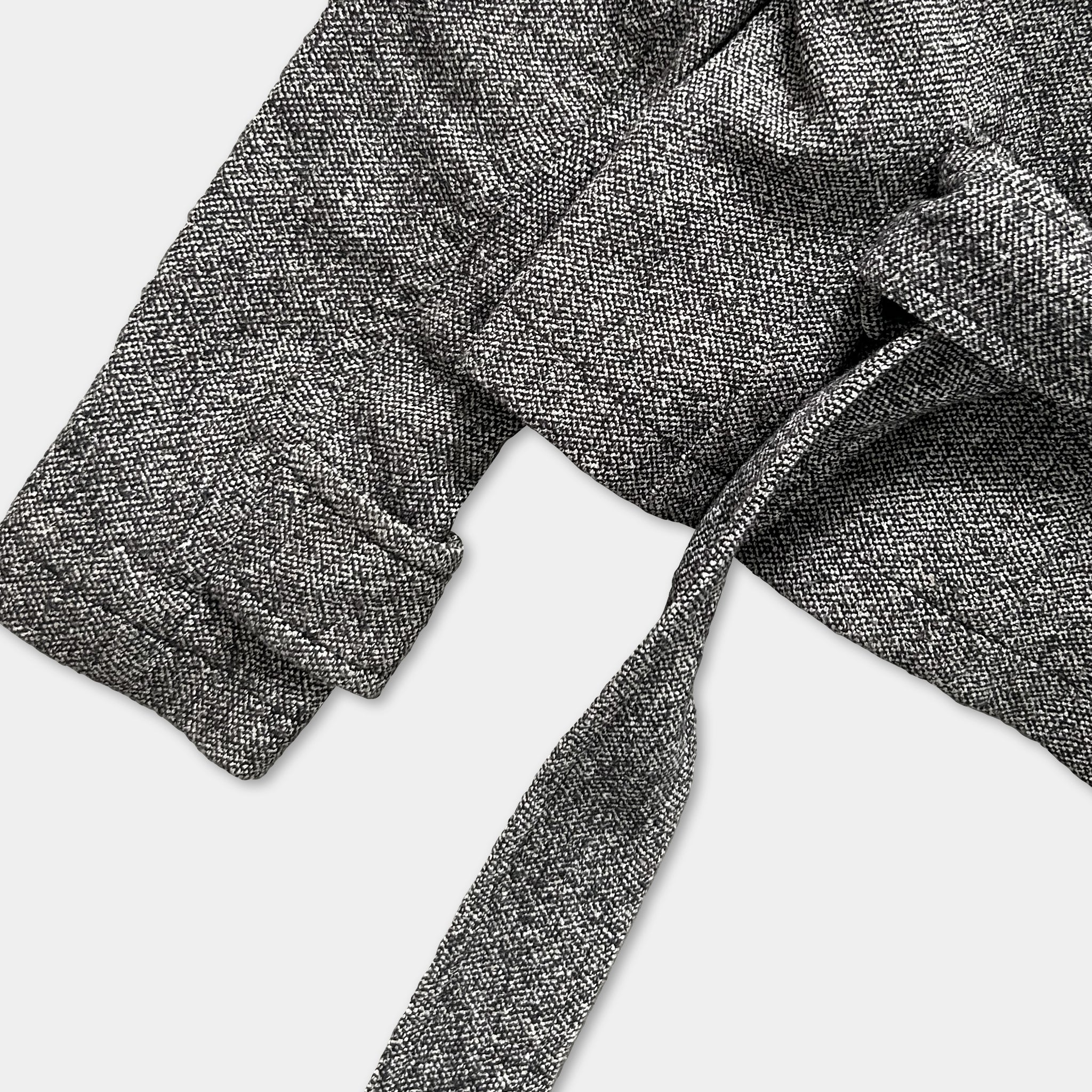 A close-up view of a grey tweed jacket with a tie, showing the fabric texture and the tie's knot.