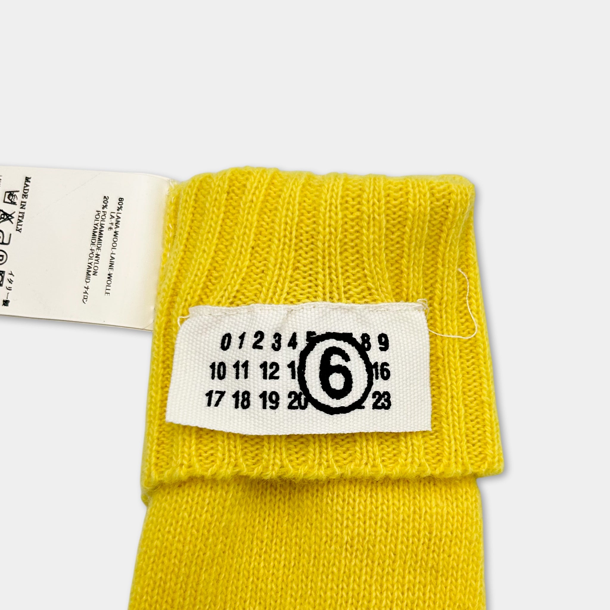 A yellow knitted sock with a label attached to it, displaying the number 6.
