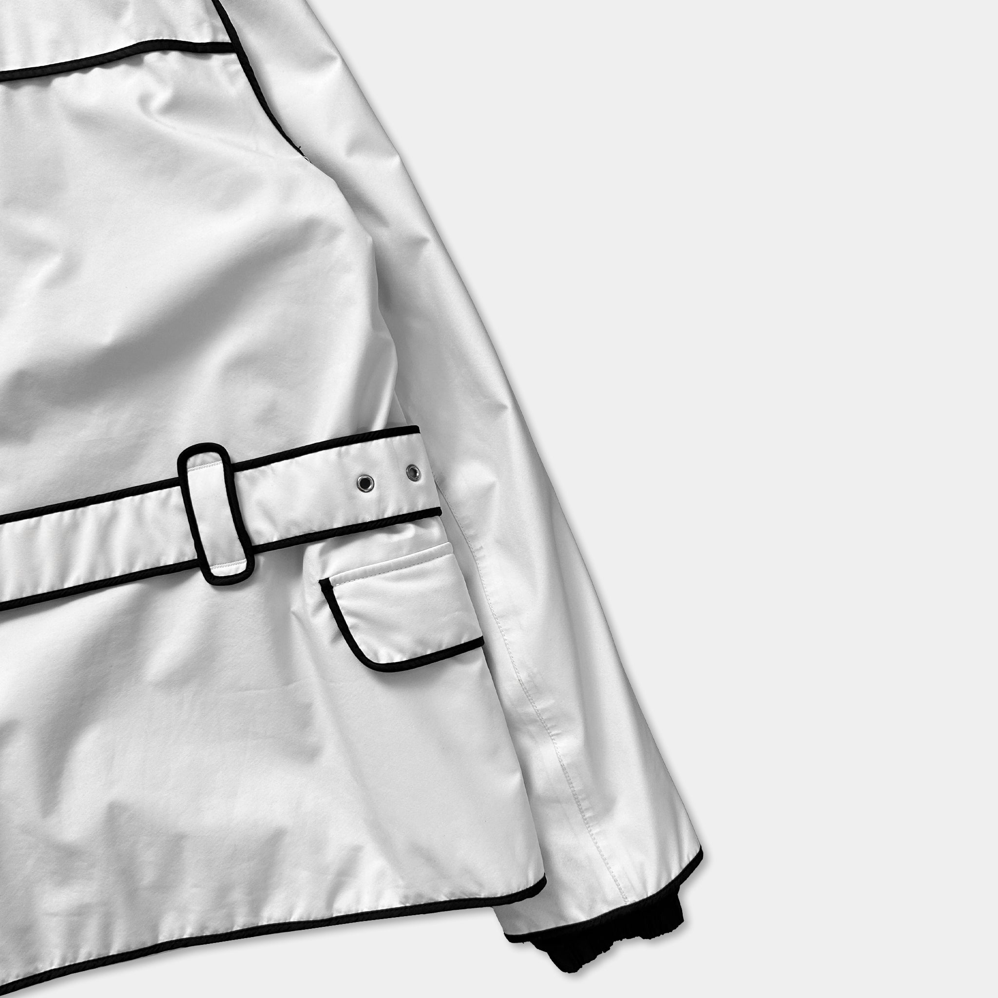 A close-up view of a white jacket with a black trim, showing the lapel, belt, and pocket.