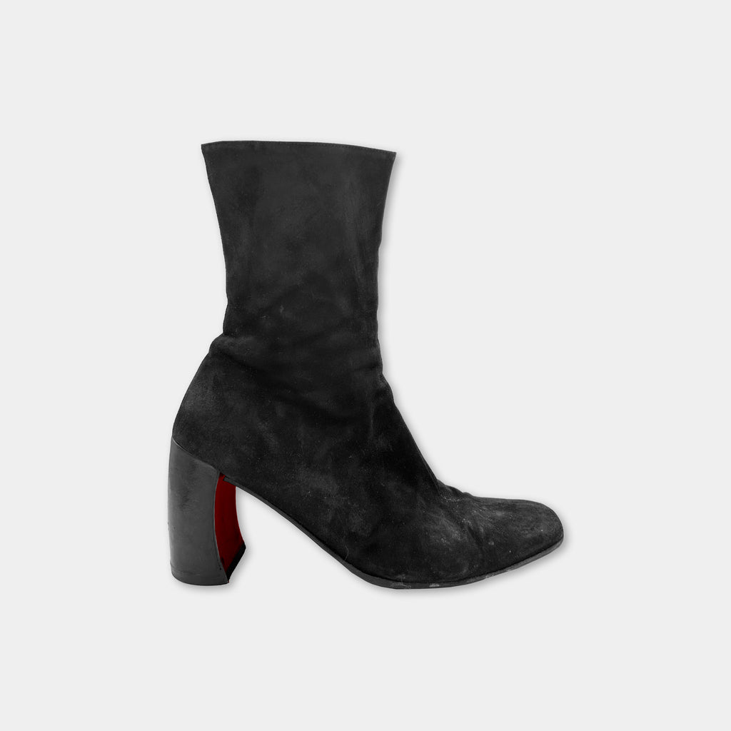 A single black suede ankle boot with a red accent detail on the heel.