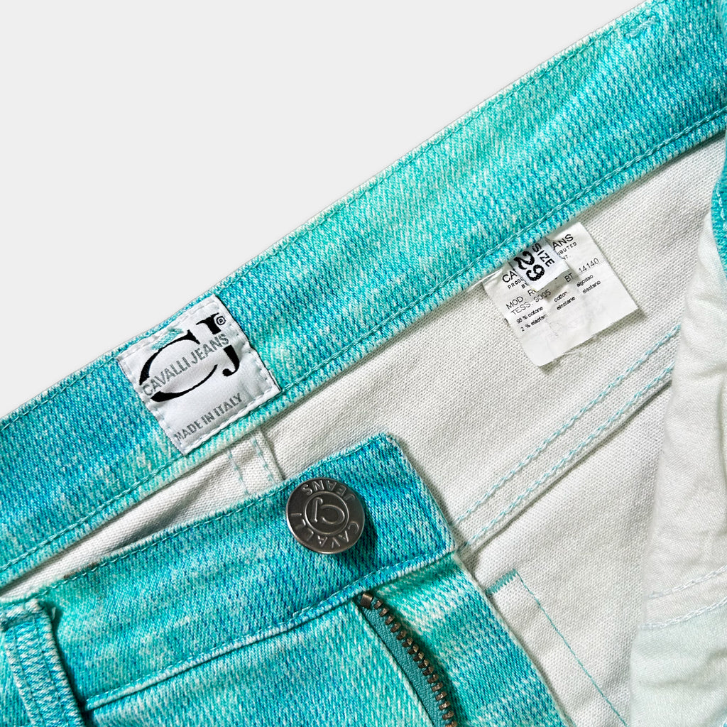 A close-up view of a pair of turquoise-colored jeans, with a label on the waistband and a zipper visible.