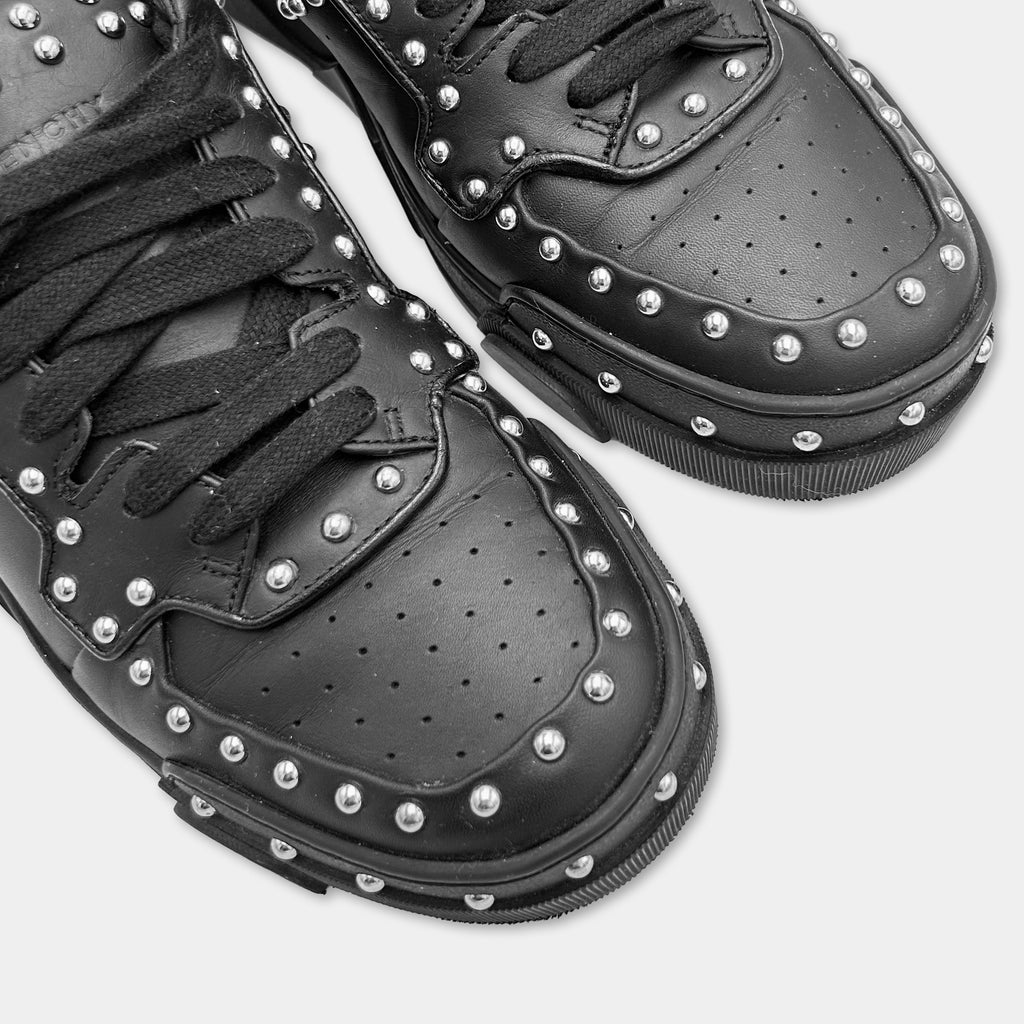 A close-up of a pair of black leather sneakers with silver studs on the top and sides.