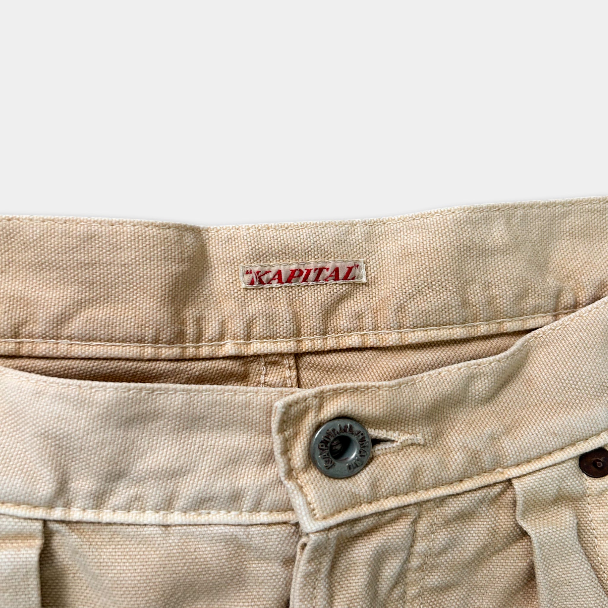 A close-up view of a pair of khaki-colored pants, with a label on the waistband that reads "CAPITAL".