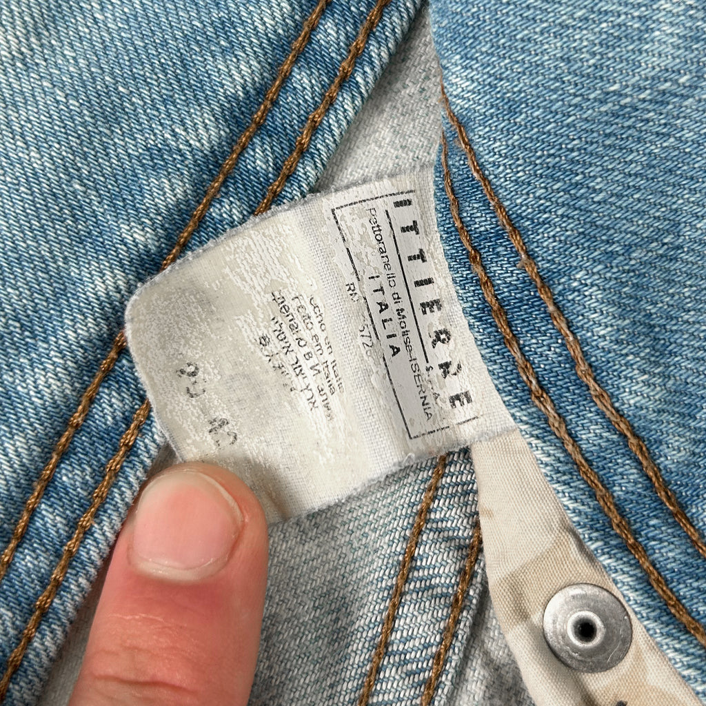A close-up view of a denim fabric, with a label attached to it, indicating the brand and size of the jeans.