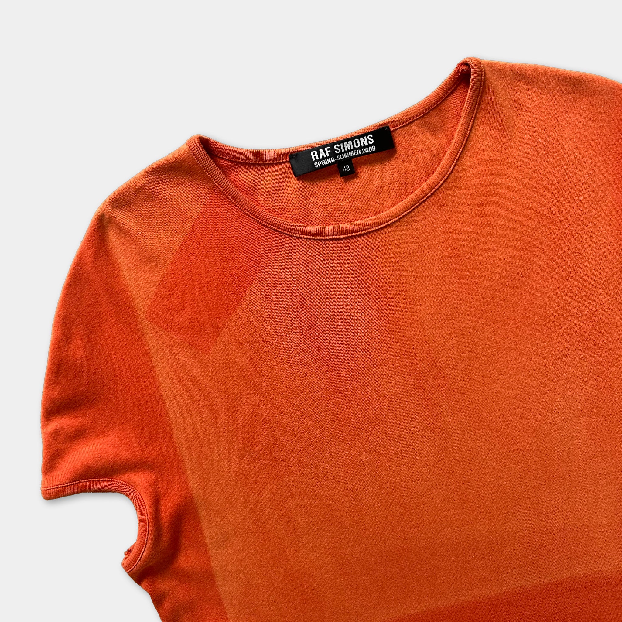 An orange t-shirt with a black label on the collar.