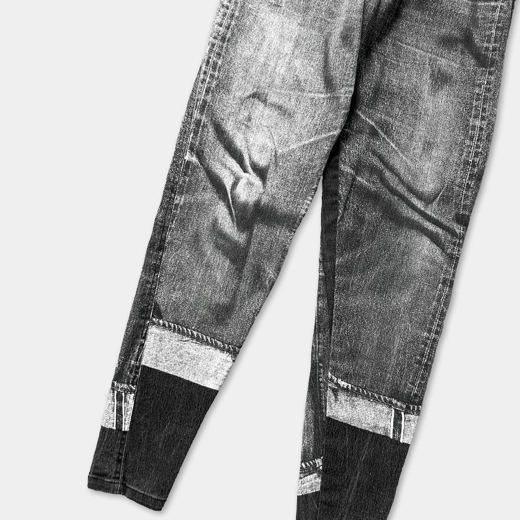 A pair of well-worn, dark-colored jeans with visible signs of wear and tear, including frayed edges and faded fabric.