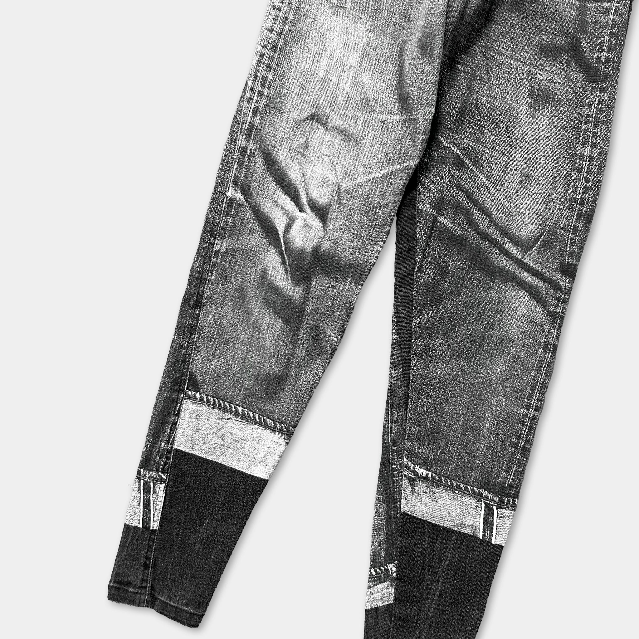 A pair of well-worn, dark-colored jeans with visible signs of wear and tear, including frayed edges and faded fabric.