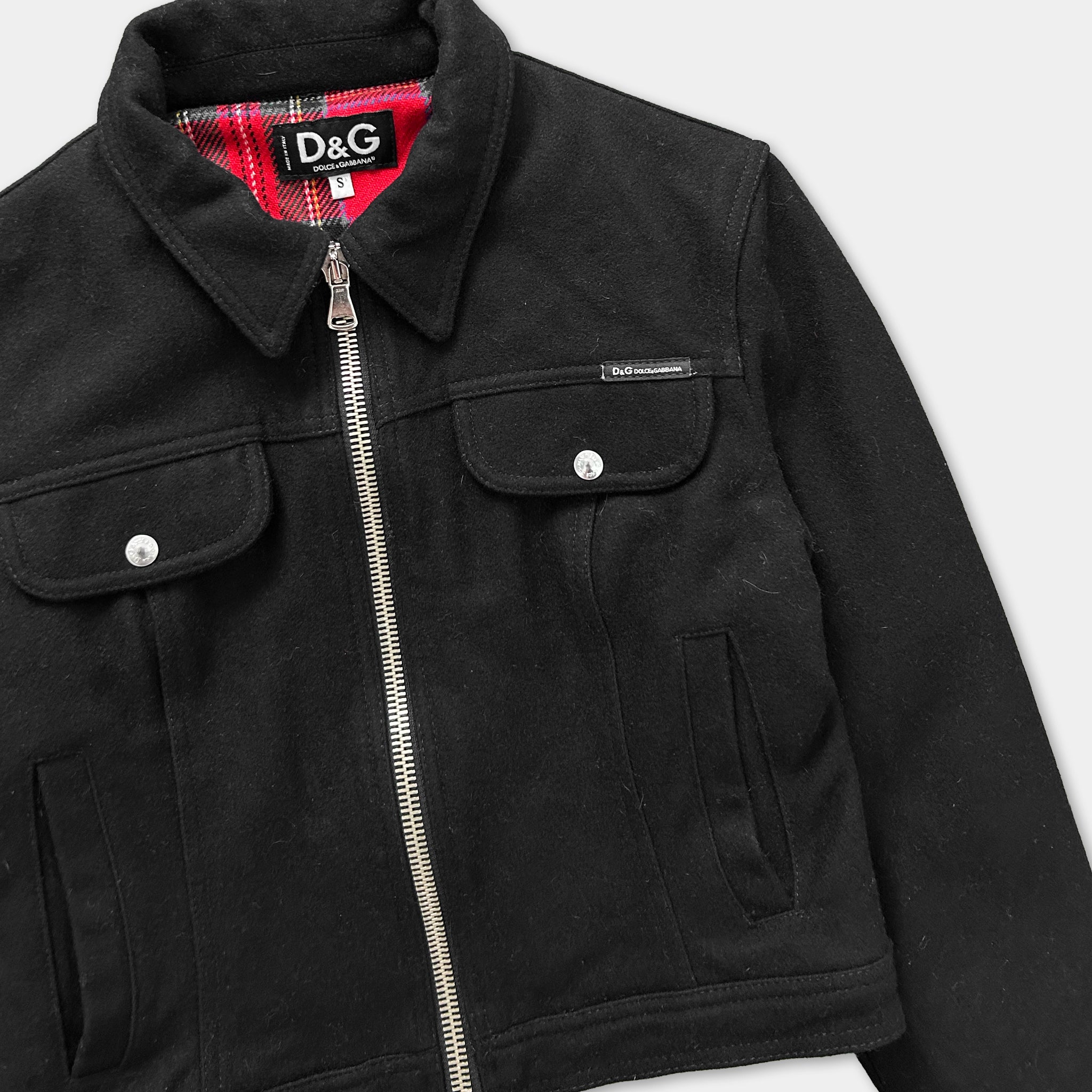 A black jacket with a zipper and pockets, featuring a red plaid lining.