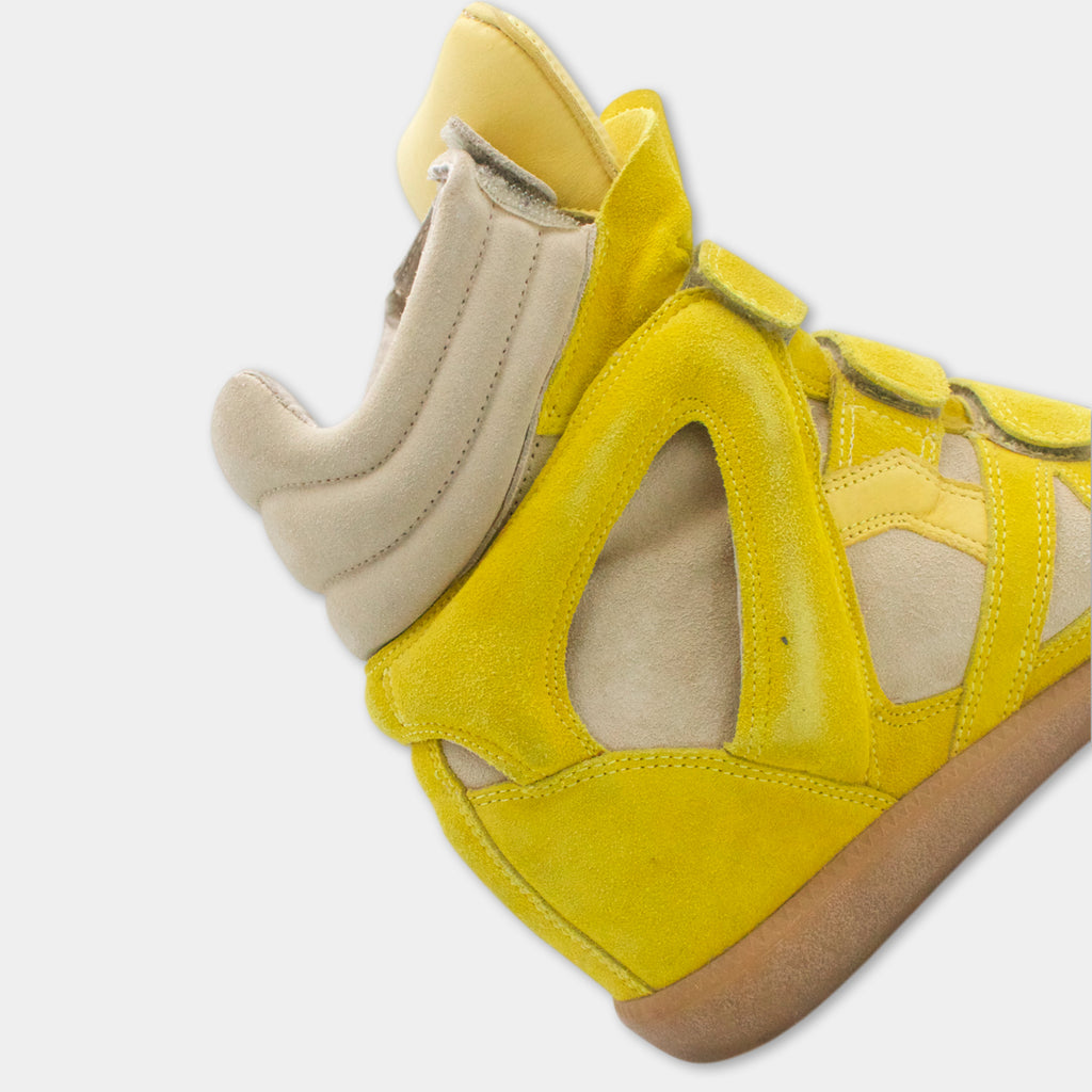 A close-up view of a yellow shoe with a beige sole and a distinctive cutout on the side.