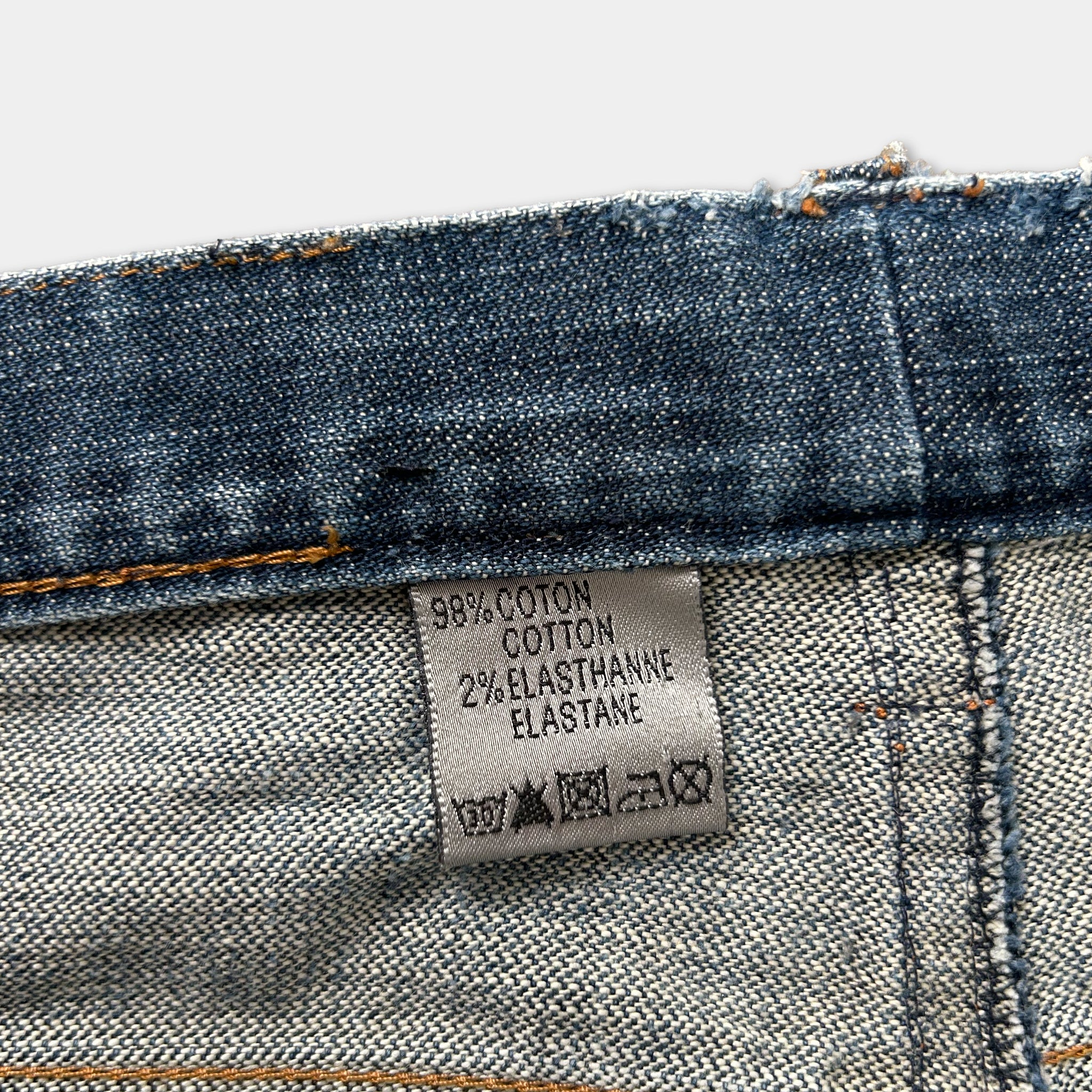 A close-up view of a denim fabric, specifically jeans, with a label attached to it. The label provides information about the fabric, such as the material and care instructions.