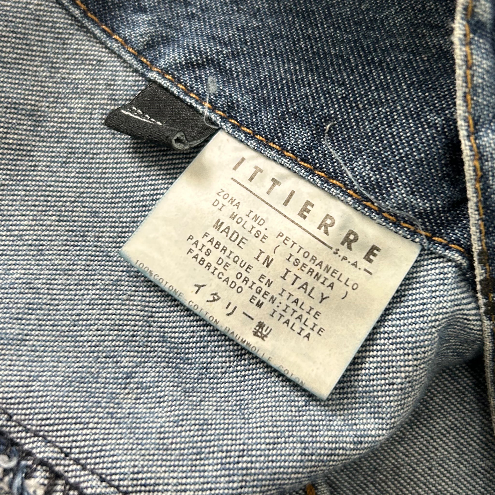 a close-up view of a denim fabric, specifically a pair of jeans, with a label attached to it. The label appears to be a label from a clothing brand, indicating that the jeans are made in Italy and are part of the brand's collection.
