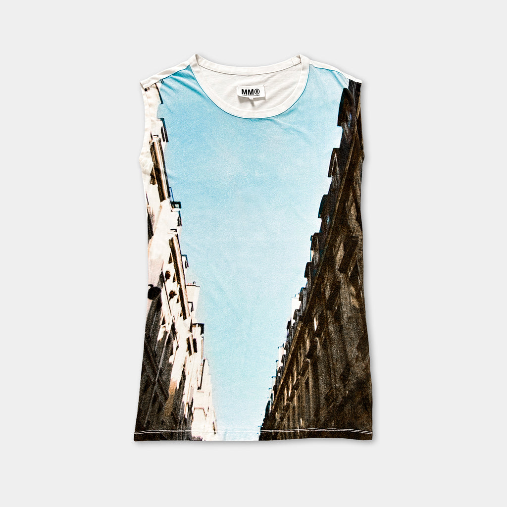 The image is a sleeveless t-shirt with a printed design depicting a cityscape with tall buildings on either side of a street.