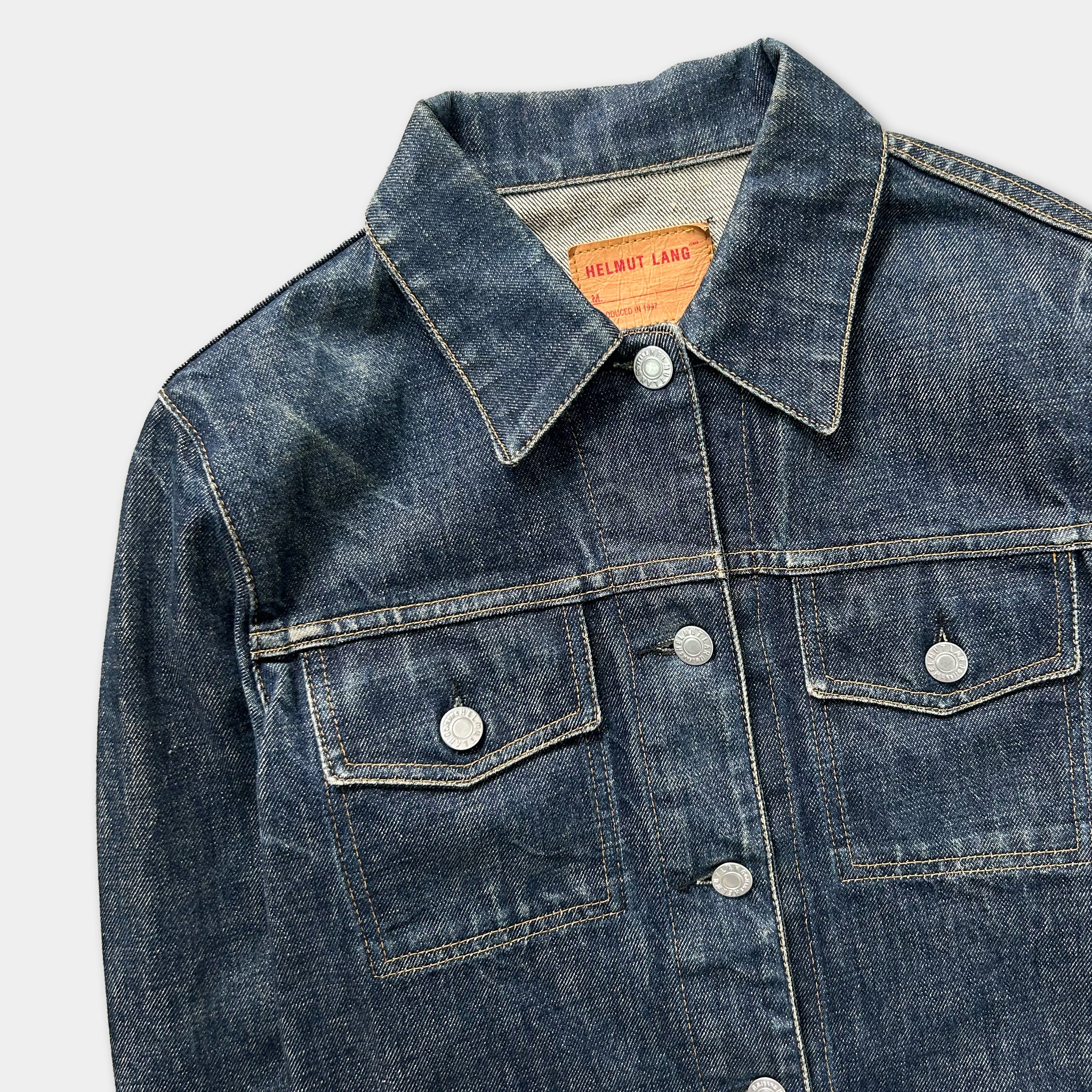 A close-up view of a blue denim jacket with a collar, buttons, and pockets.