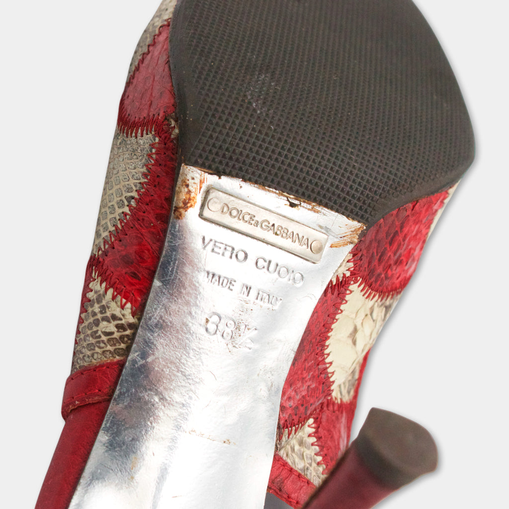 A close-up of a red and white high-heel shoe with a metal heel and a textured sole.