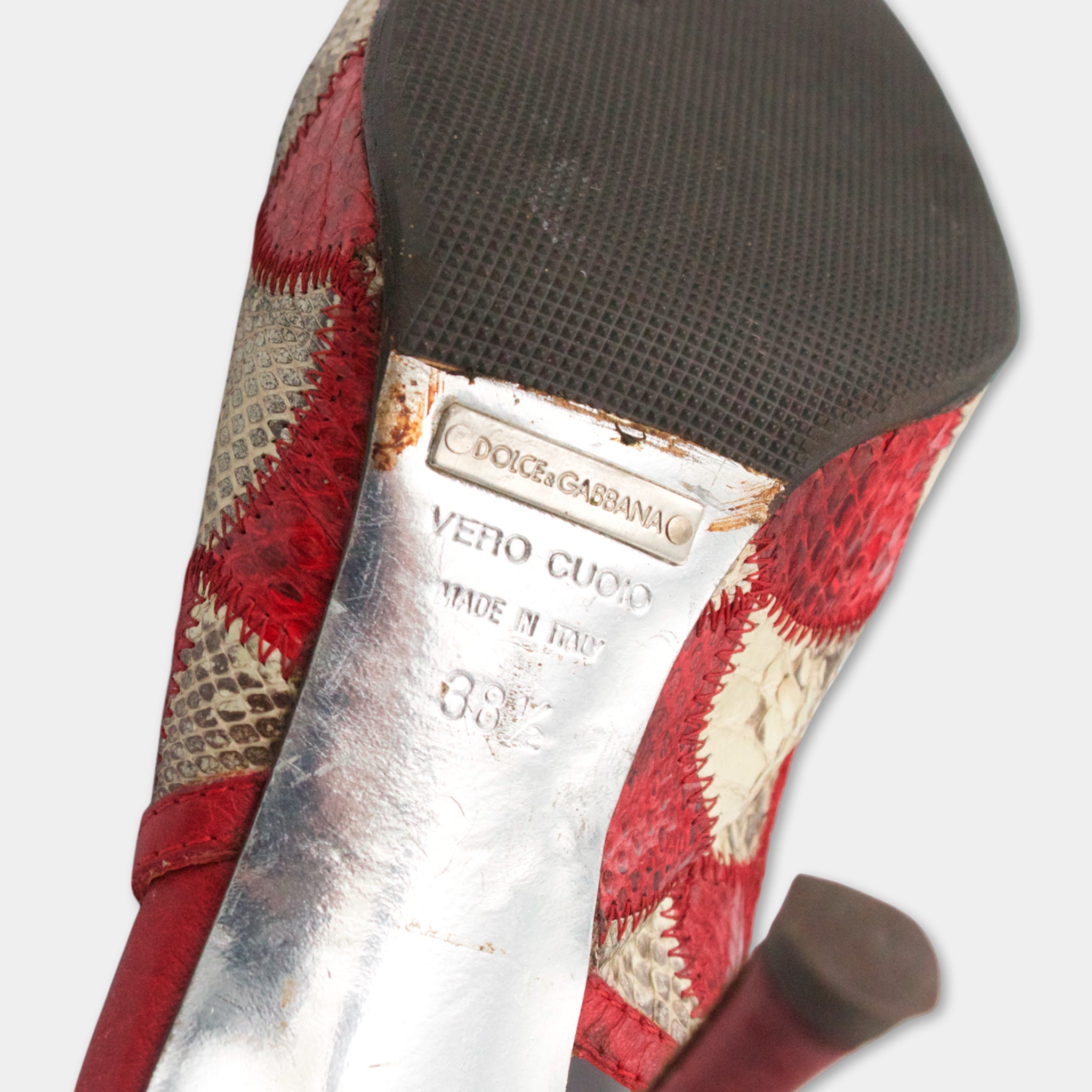 A close-up of a red and white high-heel shoe with a metal heel and a textured sole.