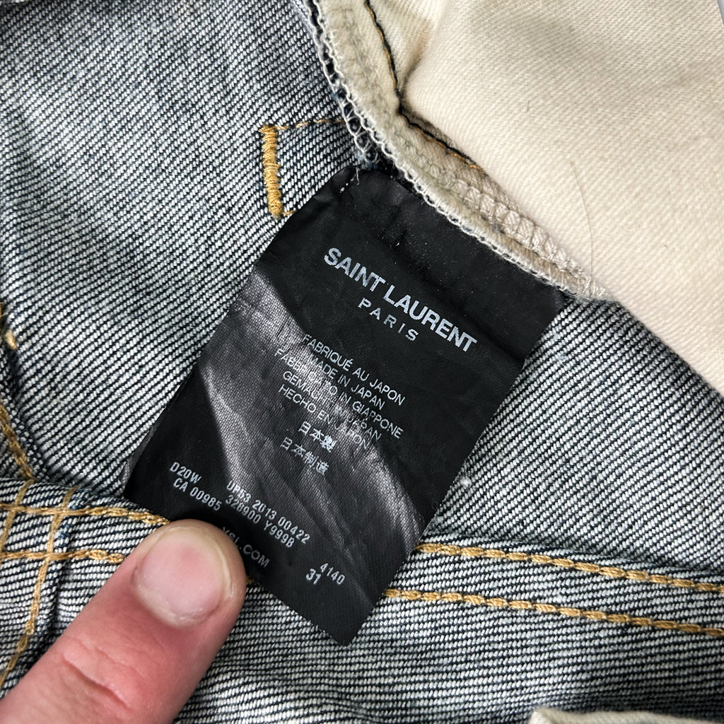 A close-up view of a black label on a pair of gray and white striped jeans, with a person's finger pointing to it.