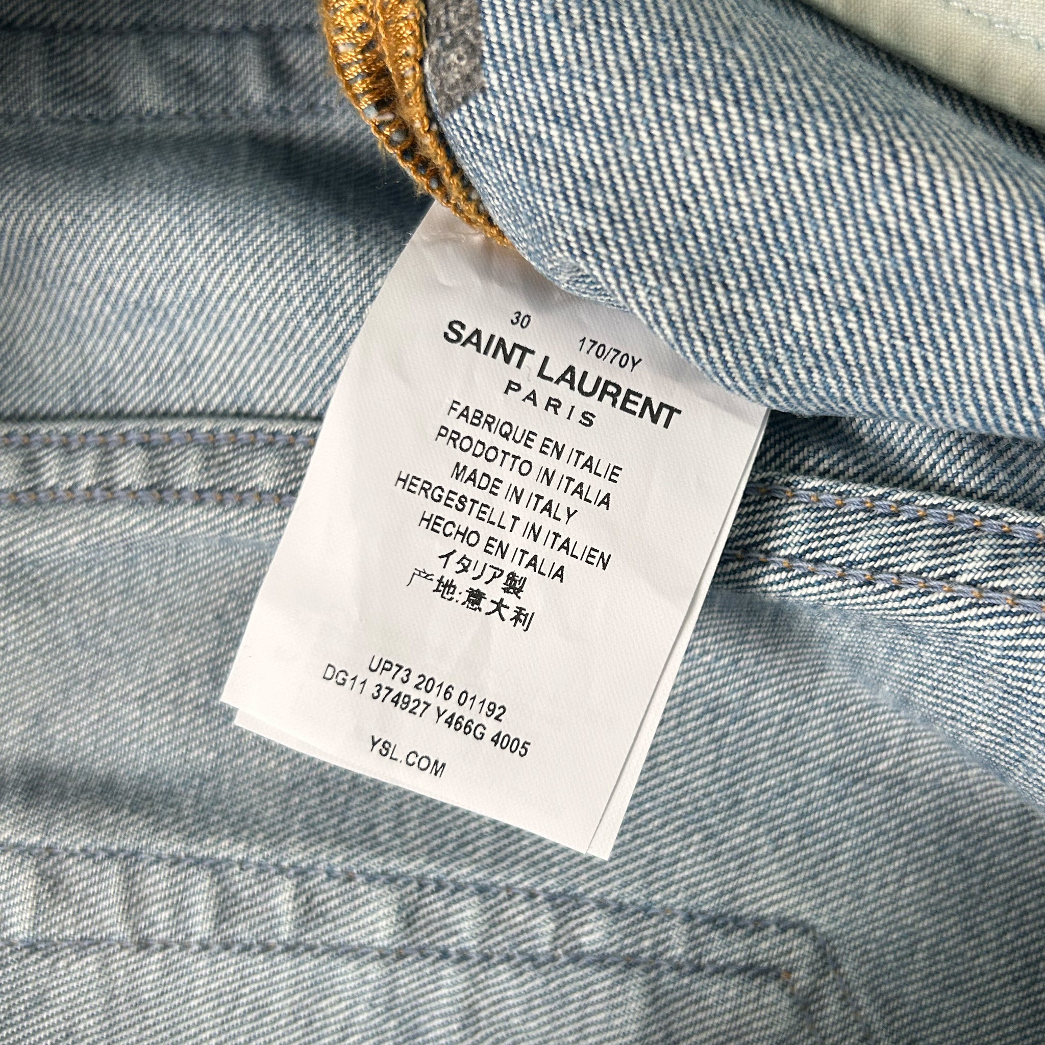 A close-up of a denim fabric, with a label attached to it, which appears to be a label from Saint Laurent.
